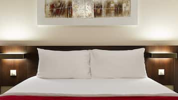 A modern hotel room with a large bed, two bedside tables, and a wall-mounted abstract painting.