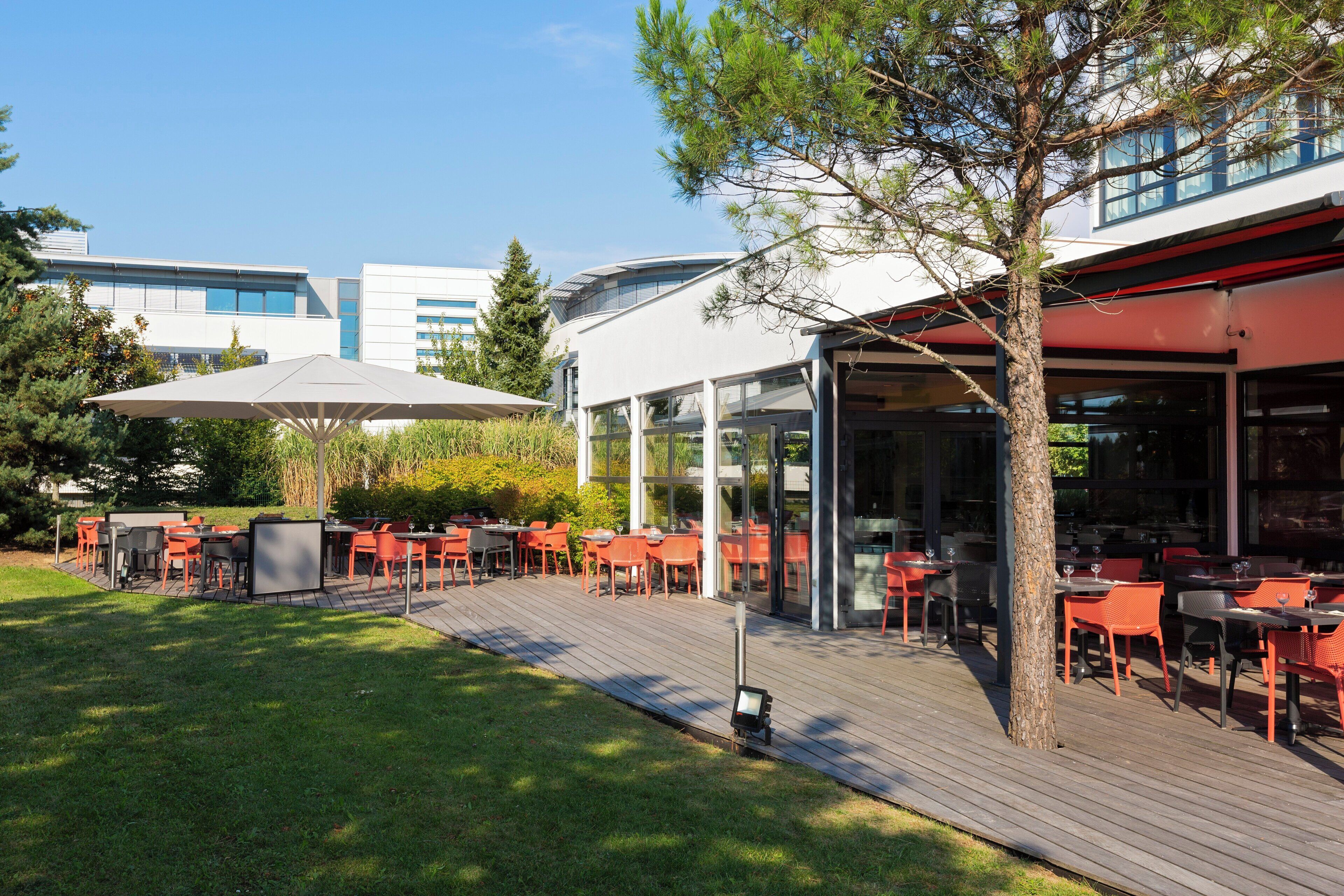 An outdoor dining area with tables and chairs, a covered seating area, and a building in the background.