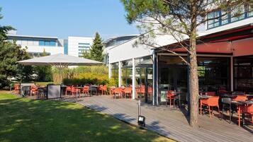 An outdoor dining area with tables and chairs, a covered seating area, and a building in the background.