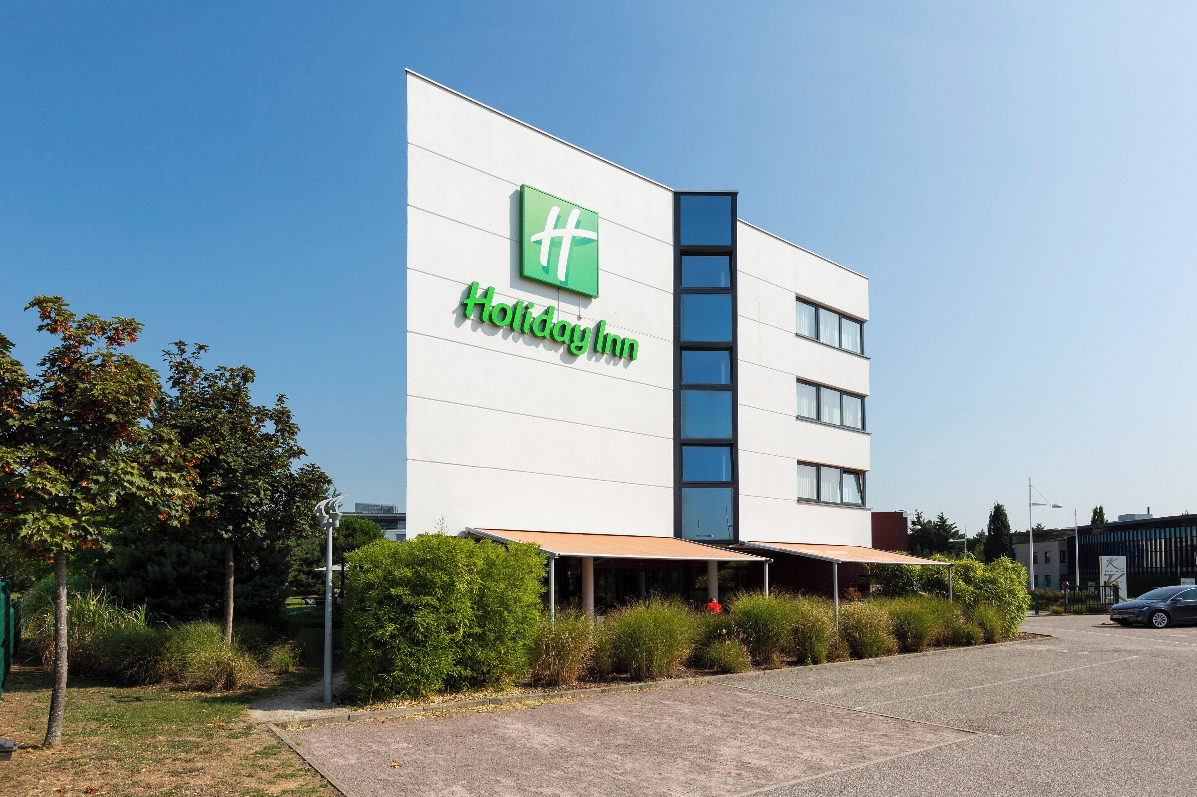 A Holiday Inn hotel with a modern design, featuring a prominent green logo and the name on the facade.