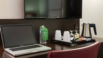 A hotel room with a laptop on a desk, a bottle of water, a tray with cups and a coffee maker.