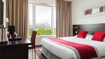 A hotel room with a bed, a desk, a chair, and a window with curtains.