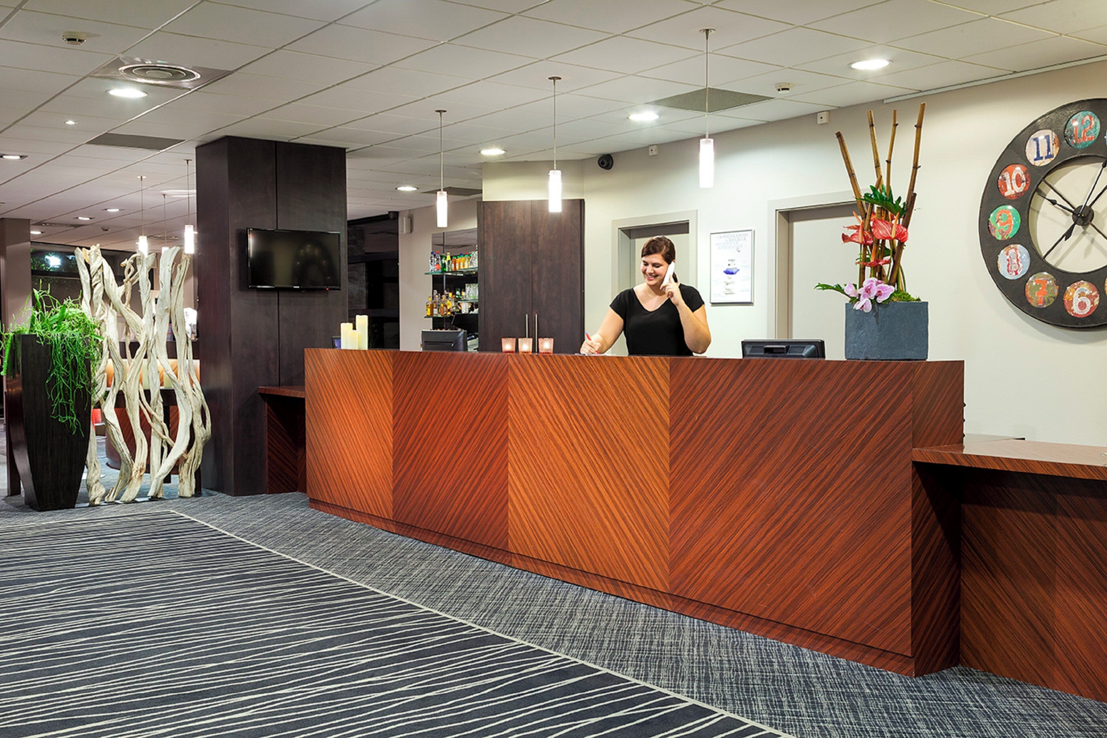 Un taulell de recepció de disseny modern, un rellotge a la paret i una planta decorativa.