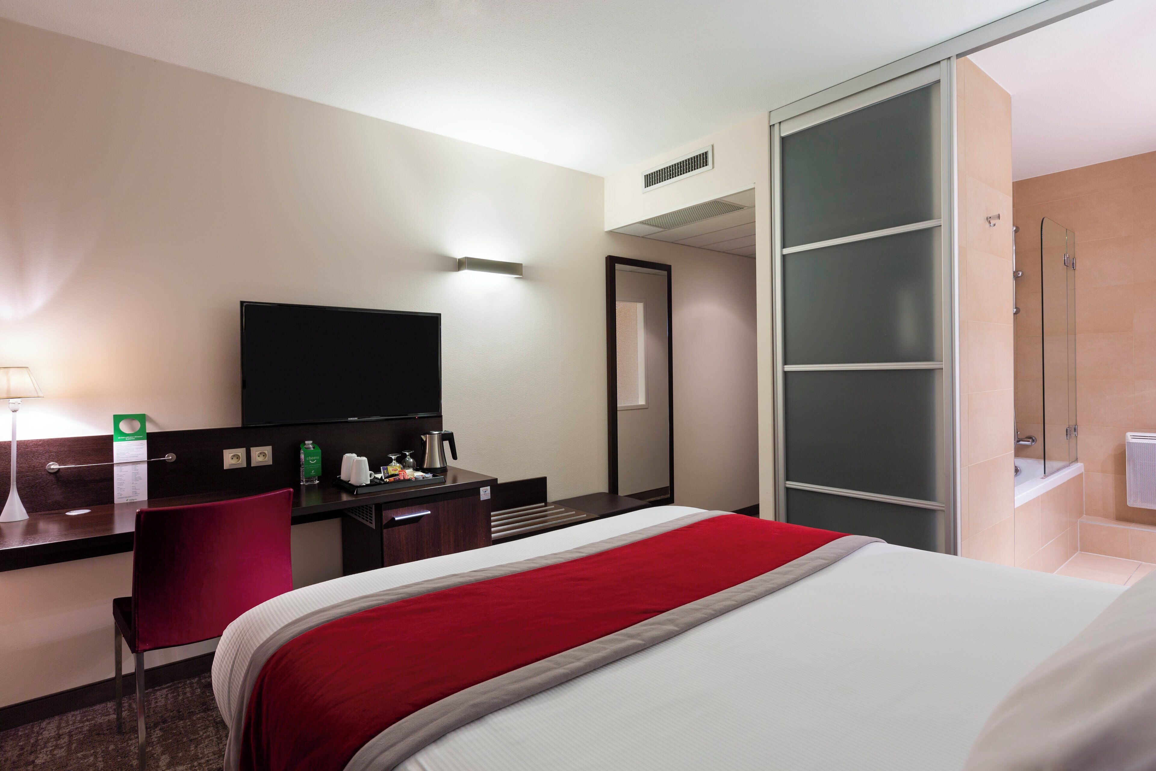Una habitación de hotel con cama, escritorio, silla, televisor y armario.