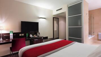 Una habitación de hotel con cama, escritorio, silla, televisor y armario.