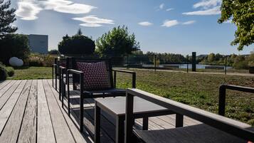 A wooden deck with outdoor seating, a view of a lake, and a building in the background.