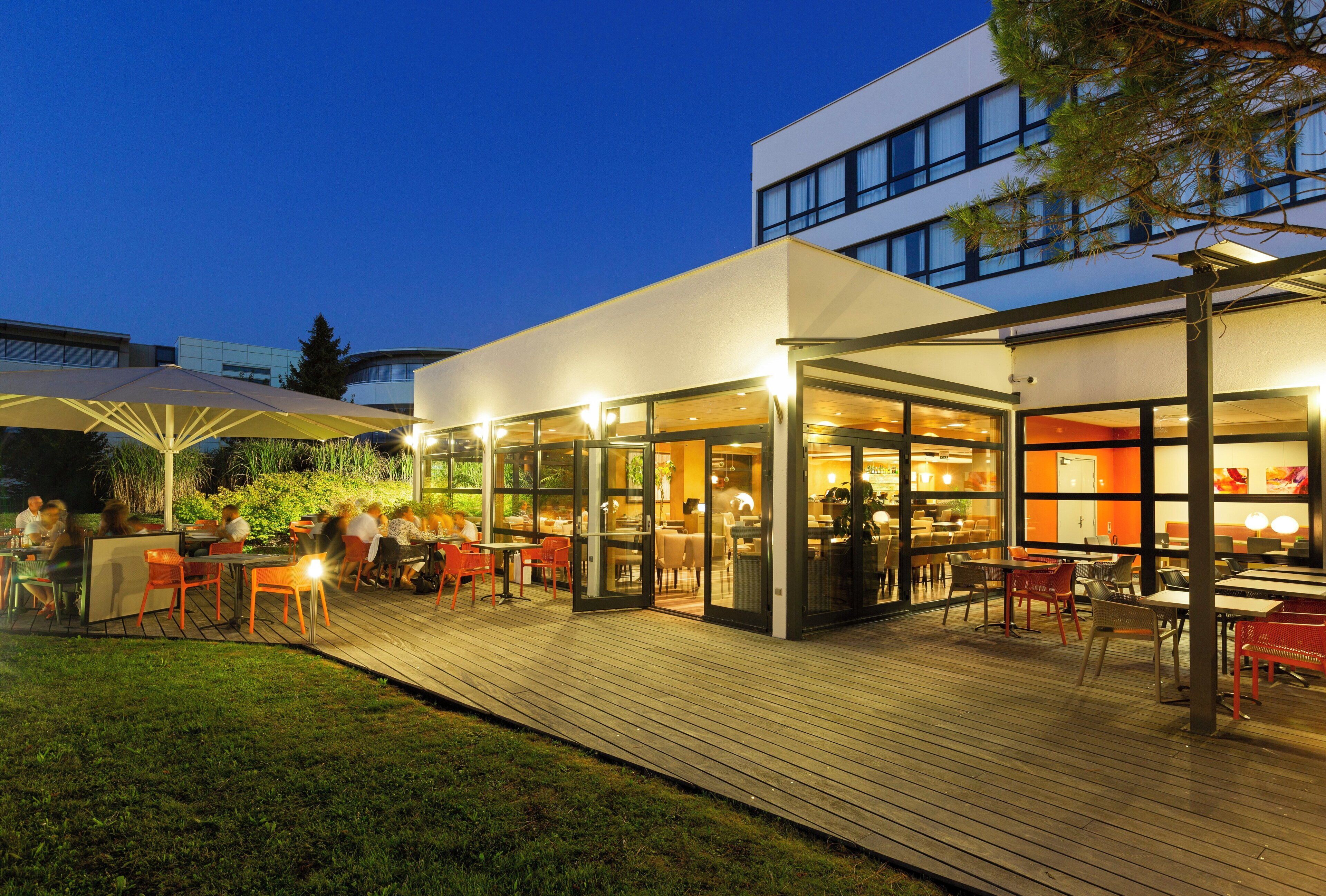 An outdoor dining area with tables and chairs, connected to an indoor space with glass walls.