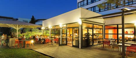 An outdoor dining area with tables and chairs, connected to an indoor space with glass walls.