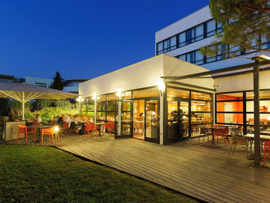 Un espace extérieur aménagé pour les repas, avec des tables et des chaises, qui est relié à un espace intérieur par des murs en verre.