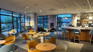Un espacio interior moderno con mesas y sillas redondas, una zona de bar y grandes ventanales que ofrecen vistas al exterior.