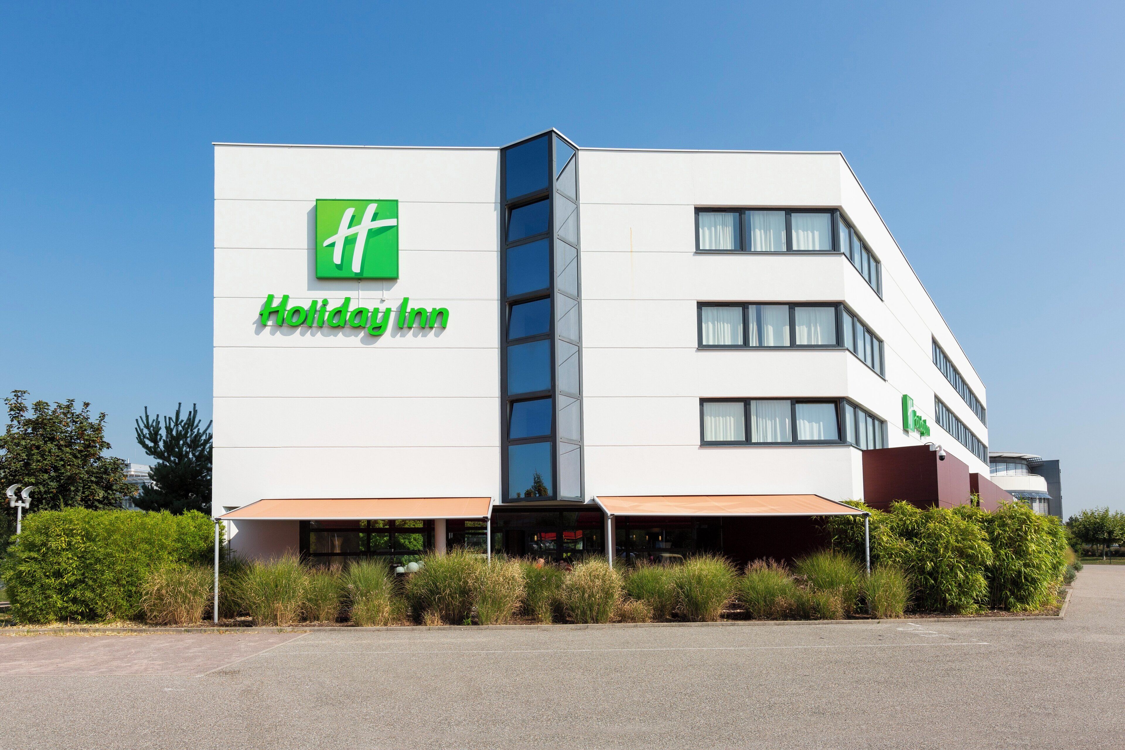 Edificio de un hotel Holiday Inn con un logo verde llamativo, múltiples ventanas y un techo plano.