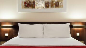 A hotel room with a large bed, two bedside lamps, and a wall-mounted artwork.