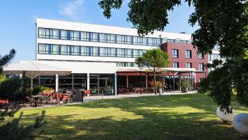 Un bâtiment moderne doté d’un espace extérieur aménagé, partiellement abrité, et d’une cour verdoyante.
