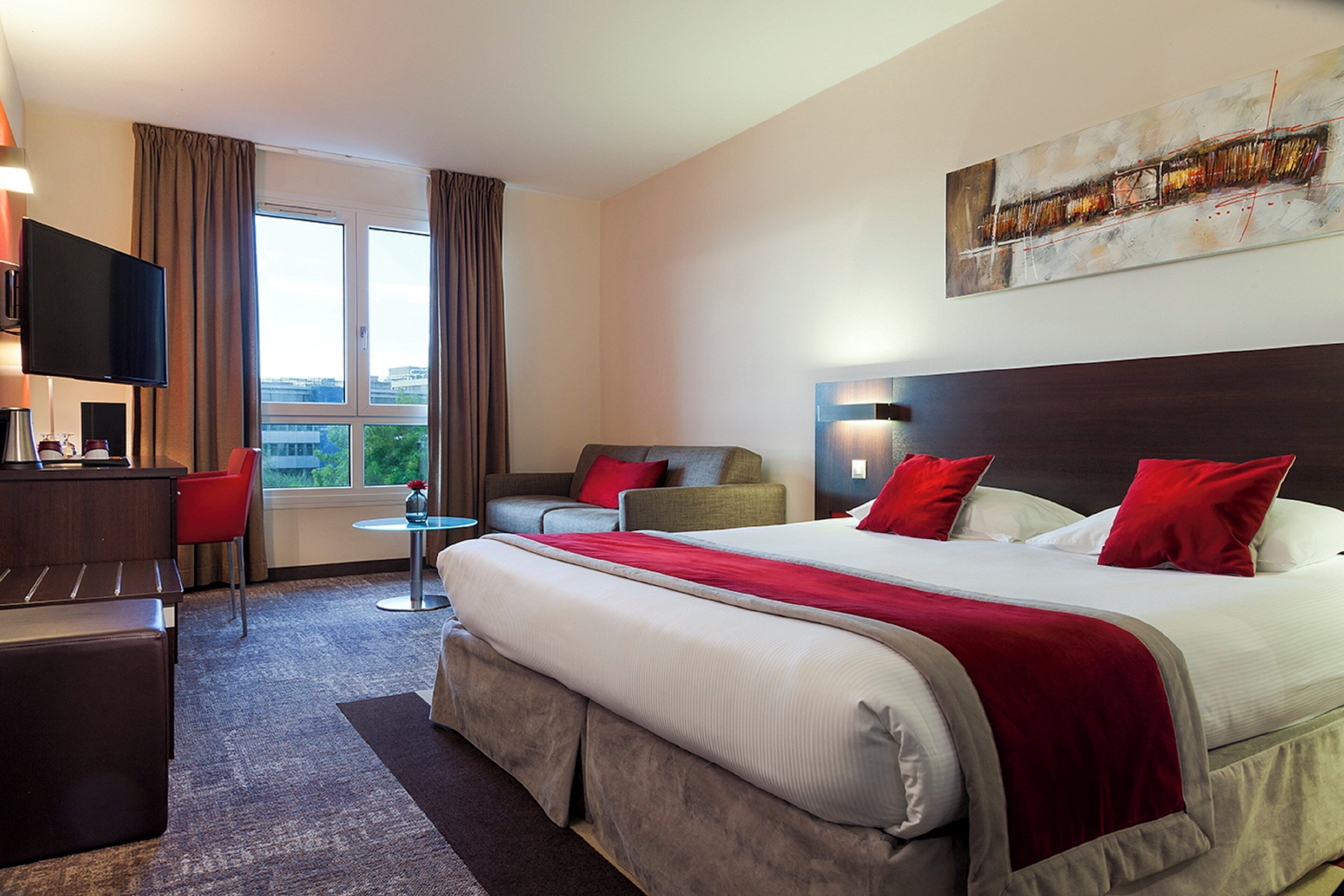 A hotel room with a large bed, a desk, a TV, and a window with curtains.