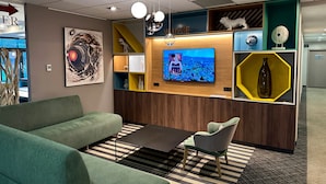 Un espacio de oficina moderno con un sofá verde, una pequeña mesa y un televisor sobre una pared de madera.