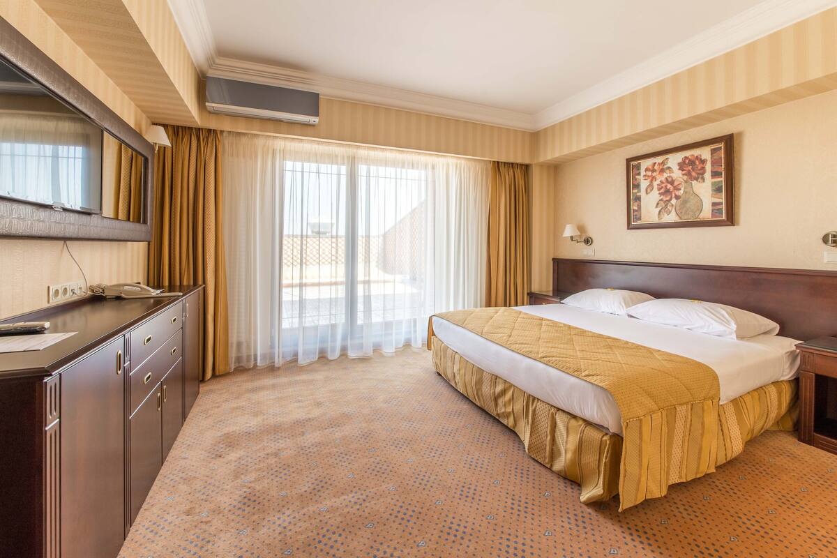 Een hotelkamer met een bed, een bureau, een stoel, een televisie en een raam met gordijnen.