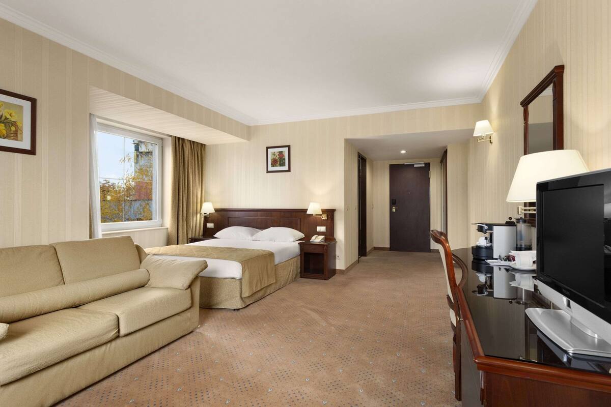 Een hotelkamer met een bed, een slaapbank, een televisie en een bureau met een lamp.