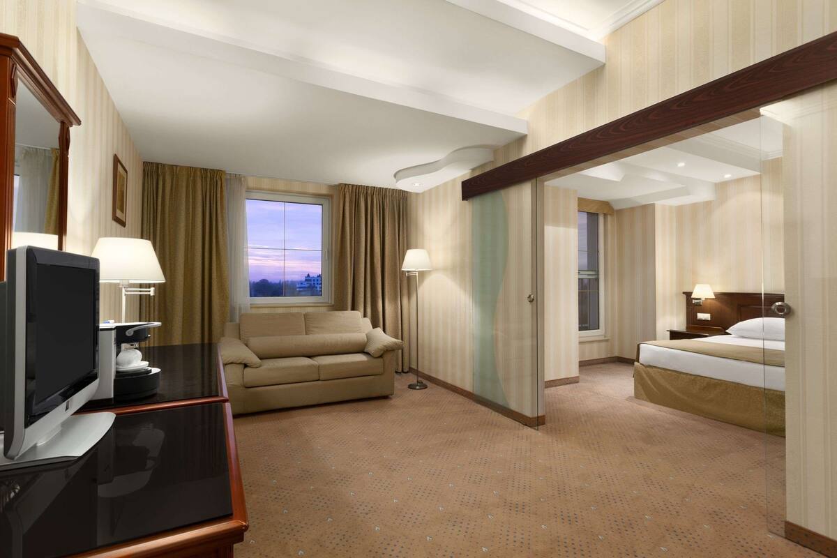 Een hotelkamer met een bed, een bank, een televisie en een raam met gordijnen.