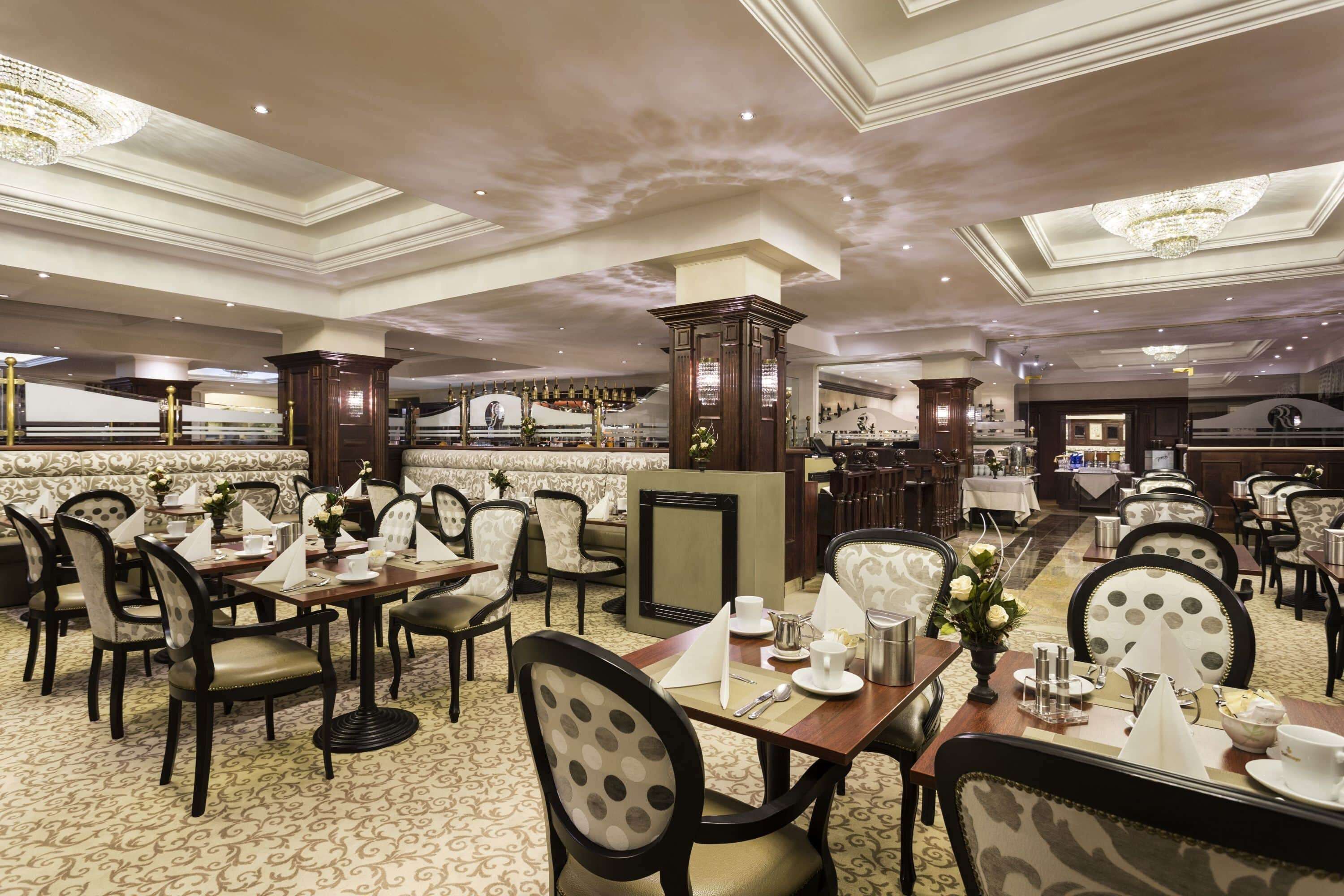 A spacious restaurant with multiple dining tables and chairs, elegant chandeliers, and a classic interior design.