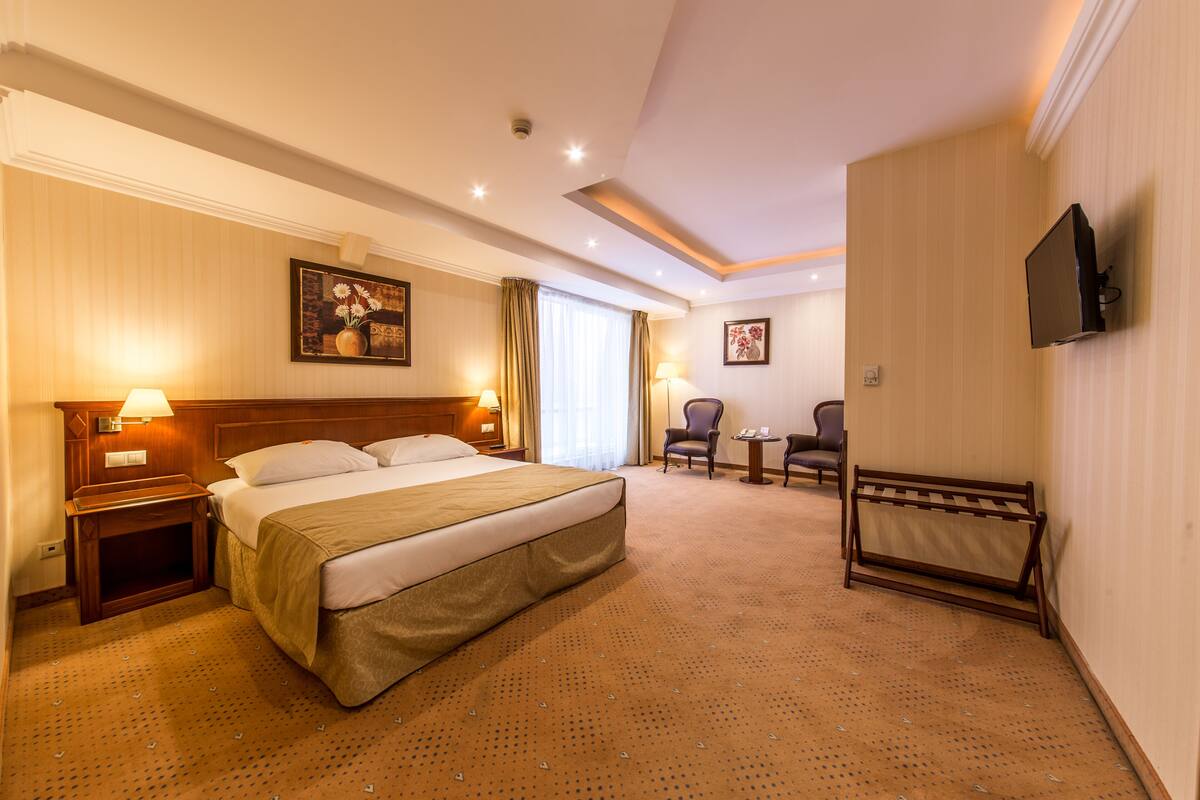 Een hotelkamer met een groot bed, nachtkastjes met lampen, een aan de muur bevestigde televisie, een zithoek met stoelen en een kleine tafel.