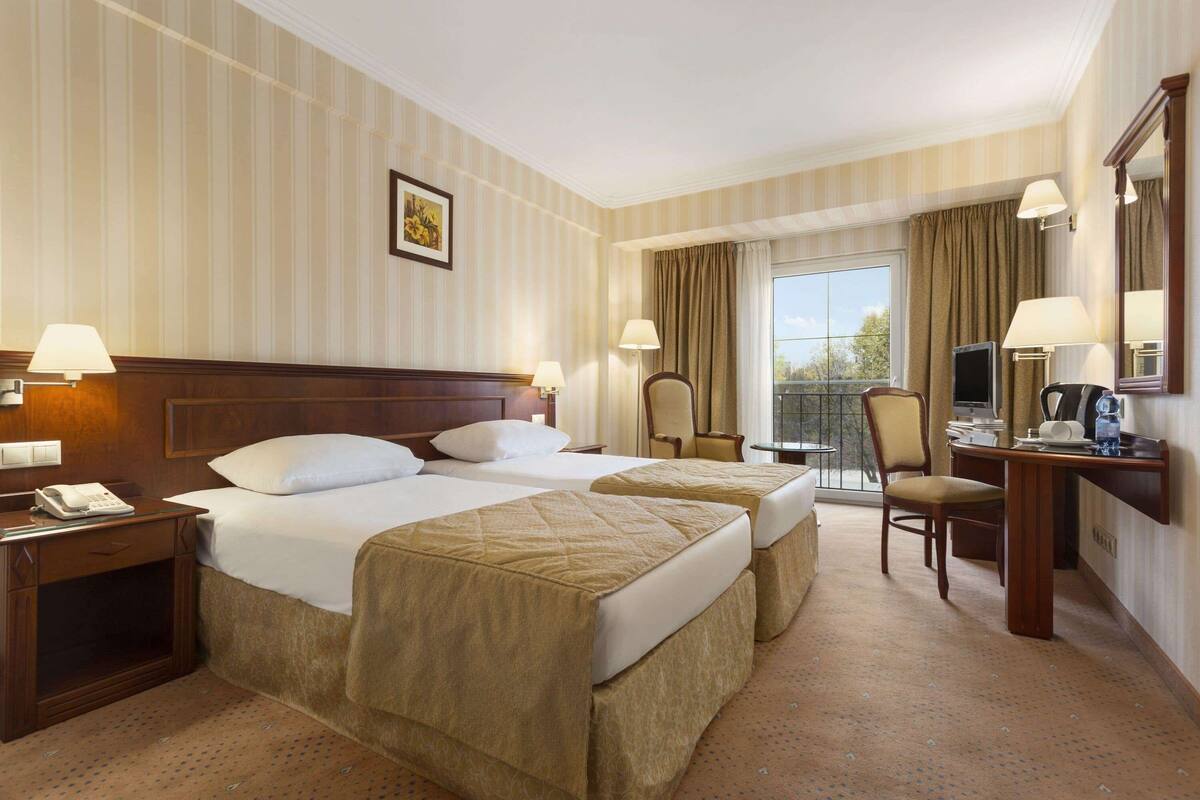 Een hotelkamer met twee bedden, een bureau, een stoel, een telefoon en een raam met gordijnen.
