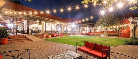 An outdoor patio area with a grassy lawn, red seating, and string lights.