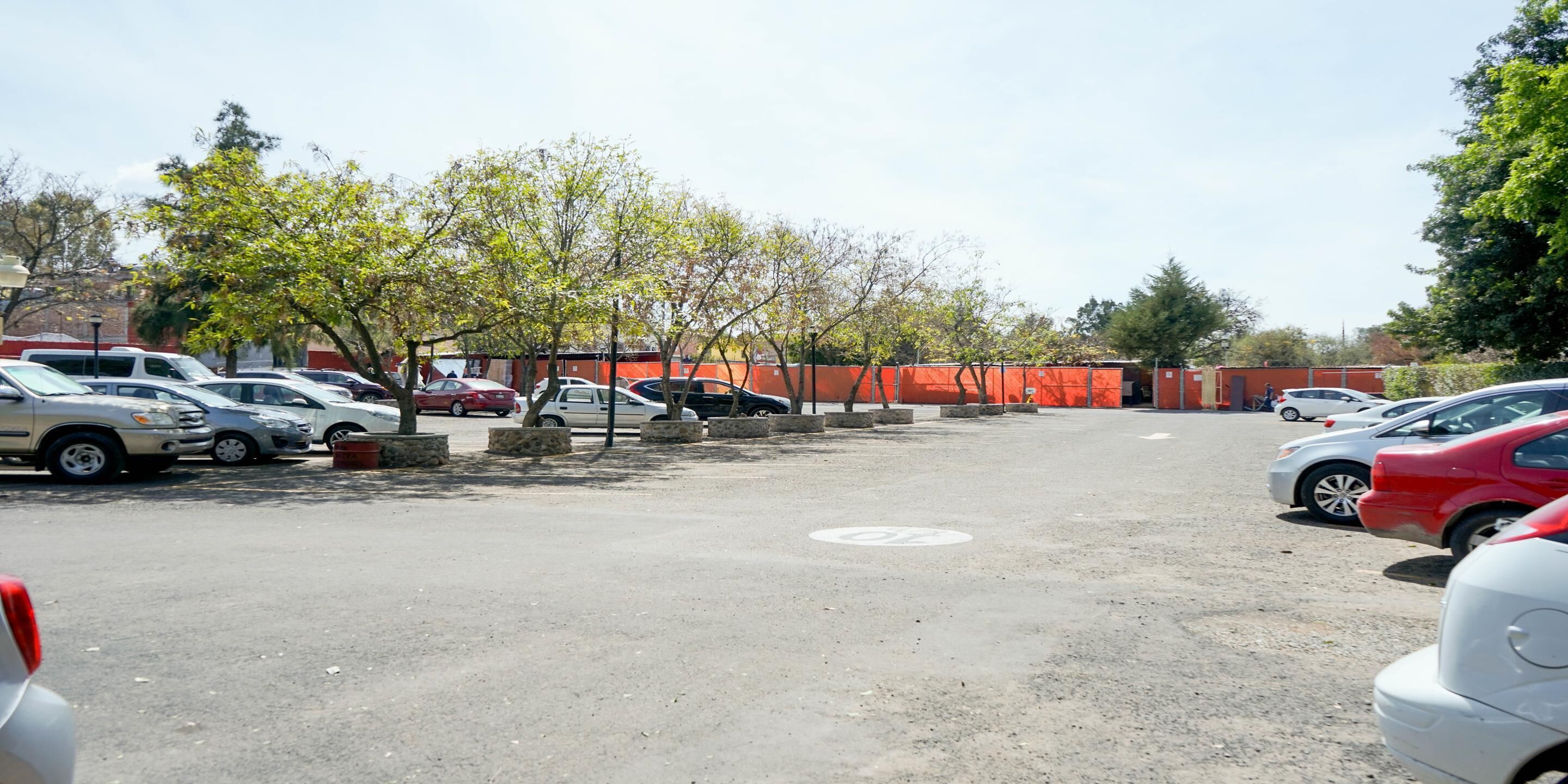 A parking lot with multiple cars, trees, and a red construction barrier.