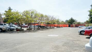Un parking avec plusieurs voitures, des arbres et une barrière de chantier rouge.