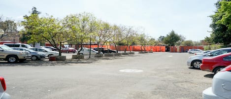 Un estacionamiento con varios coches, árboles y una barrera roja de construcción.