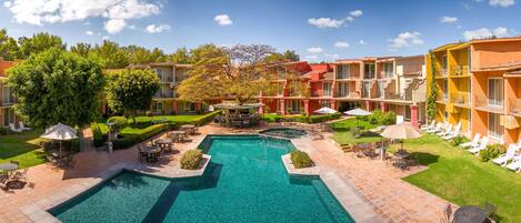 Un patio de hotel con una piscina central, zonas de estar al aire libre y un césped bien cuidado.