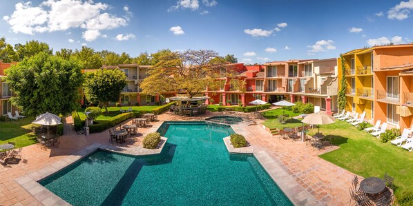Un patio de hotel con una piscina central, zonas de estar al aire libre y un césped bien cuidado.