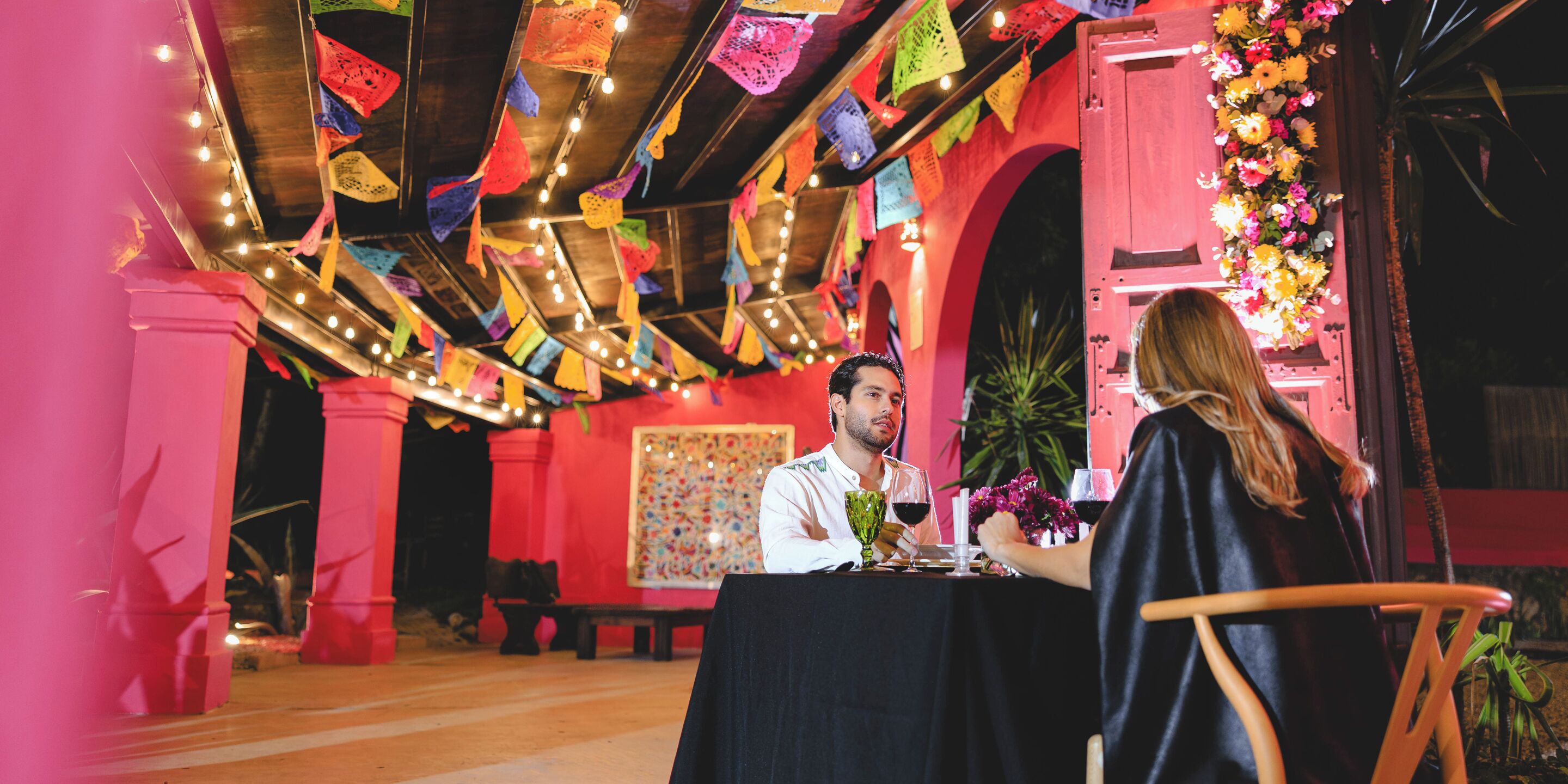 A dining area with a table set for two, a decorative ceiling, and a pink wall.