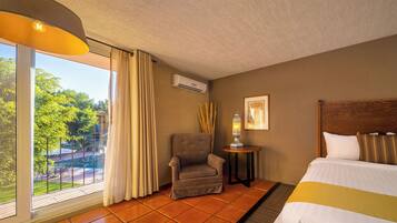 A hotel room with a bed, a chair, a small table with a lamp, and a window with curtains.