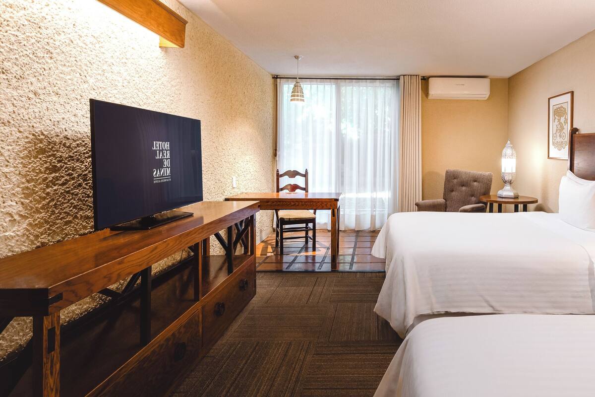 Une chambre d’hôtel avec deux lits, un bureau avec une télévision, une chaise, une lampe et une table de chevet avec un téléphone.