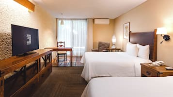 Habitación de hotel con dos camas, un escritorio con televisor, una silla, una lámpara y una mesita de noche con teléfono.