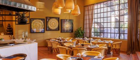 A restaurant with round tables, yellow chairs, and hanging lamps.