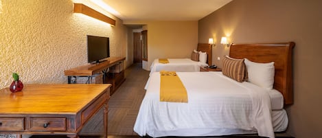 A hotel room with two beds, a TV, a wooden desk, and a wall-mounted TV.