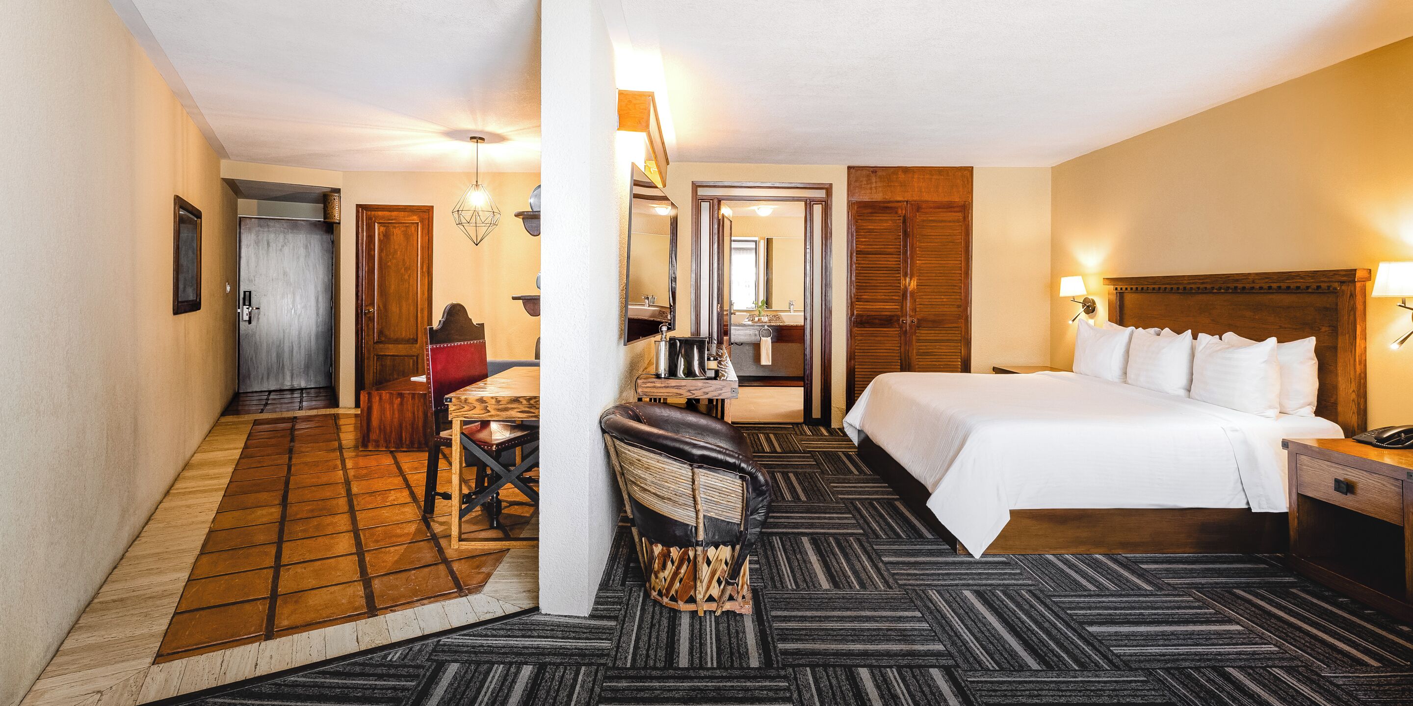 Une chambre d’hôtel comprenant un lit, un bureau avec une chaise, une salle de bain avec un miroir et une porte donnant sur une autre pièce.