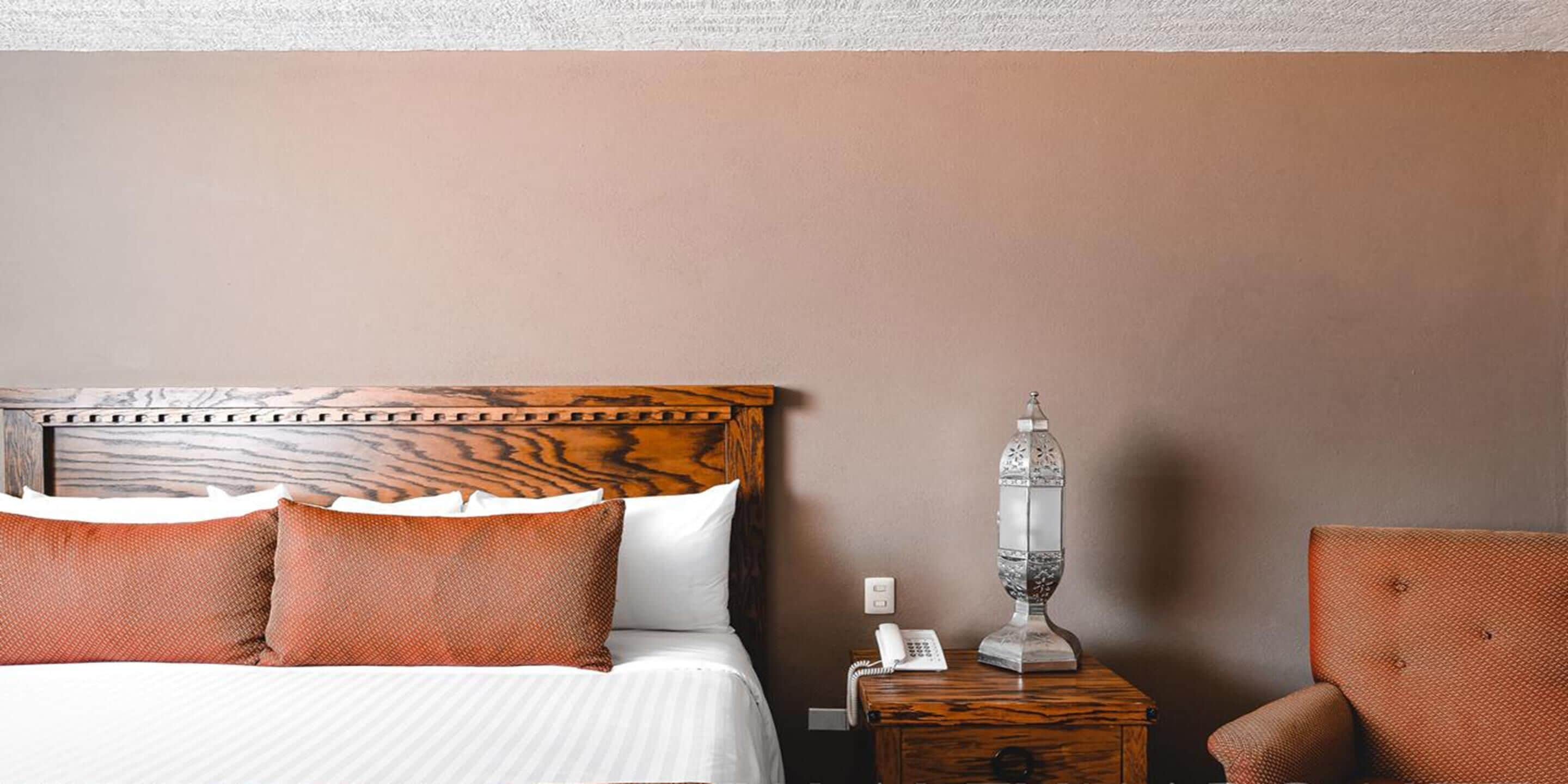 A neatly made bed with a wooden headboard, a bedside table with a lamp, and a chair.