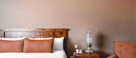 A neatly made bed with a wooden headboard, a bedside table with a lamp, and a chair.