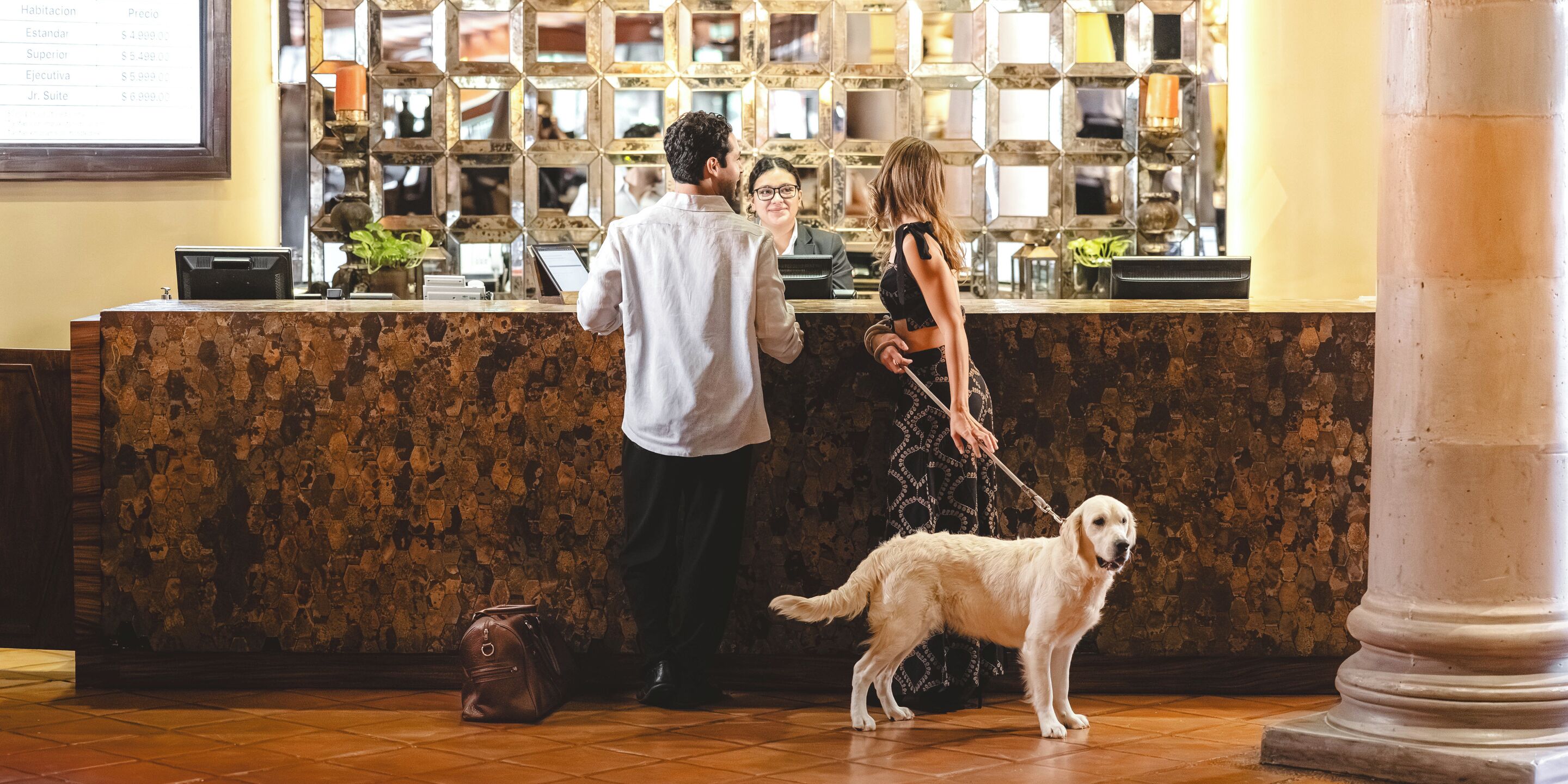 A reception area with a marble counter, a dog on a leash, and a man and woman conversing.