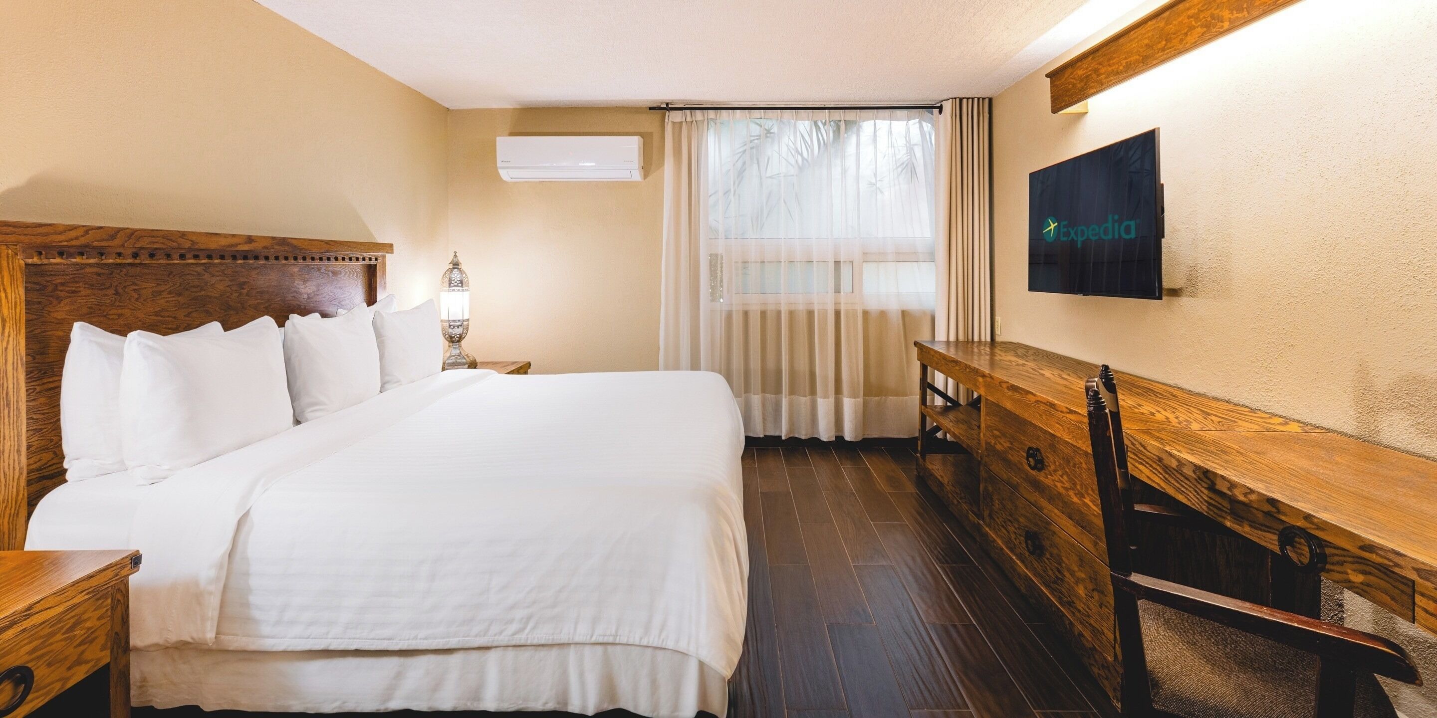 Une chambre d’hôtel avec un grand lit, une table de chevet en bois, un bureau et un téléviseur fixé au mur.