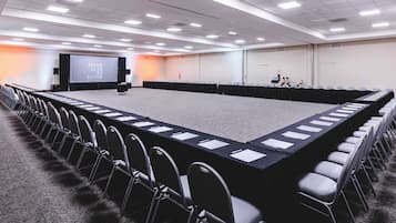 Un salón de conferencias con una larga mesa, sillas, una pantalla de proyector y piso alfombrado.