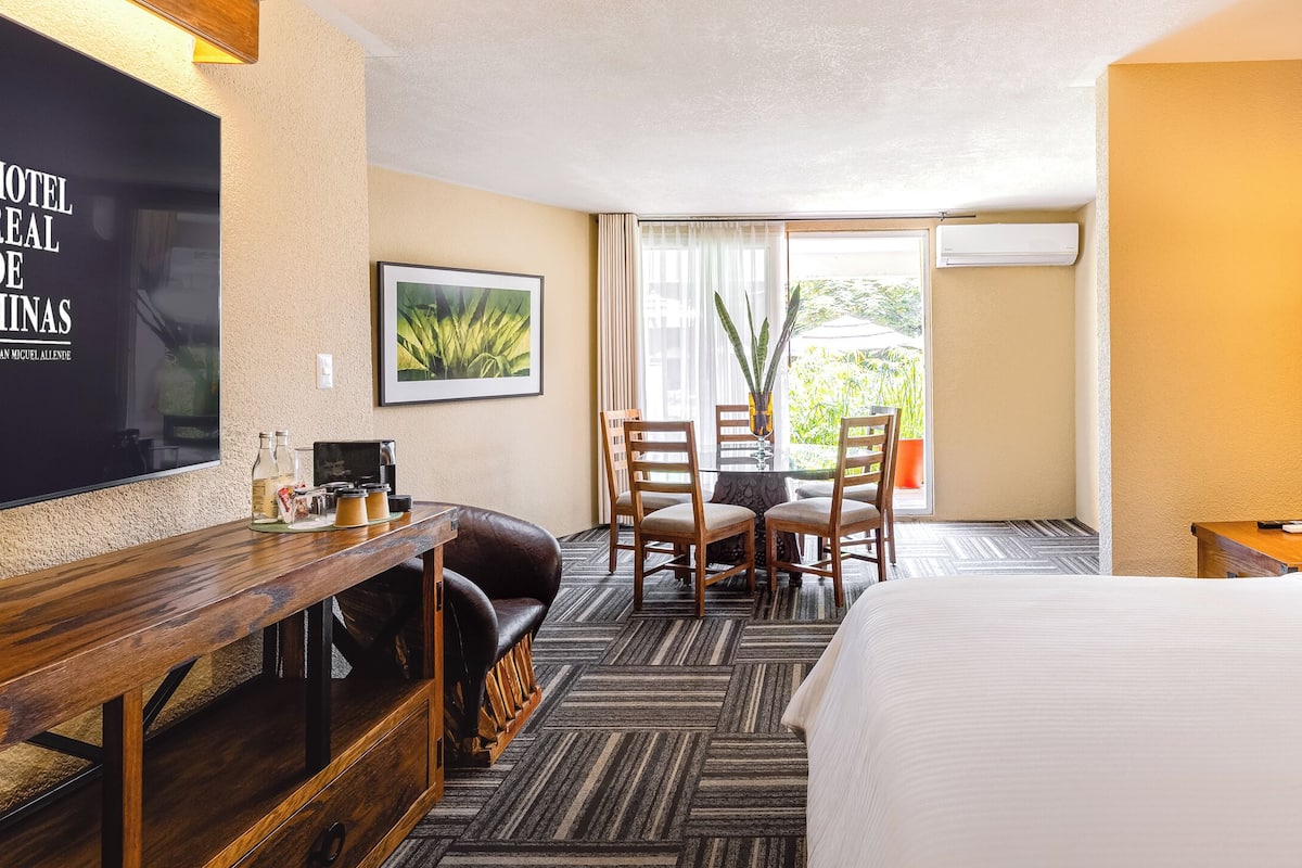 Une chambre d’hôtel comprenant un lit, un bureau avec une chaise, une télévision, un tableau encadré et une fenêtre avec des rideaux.
