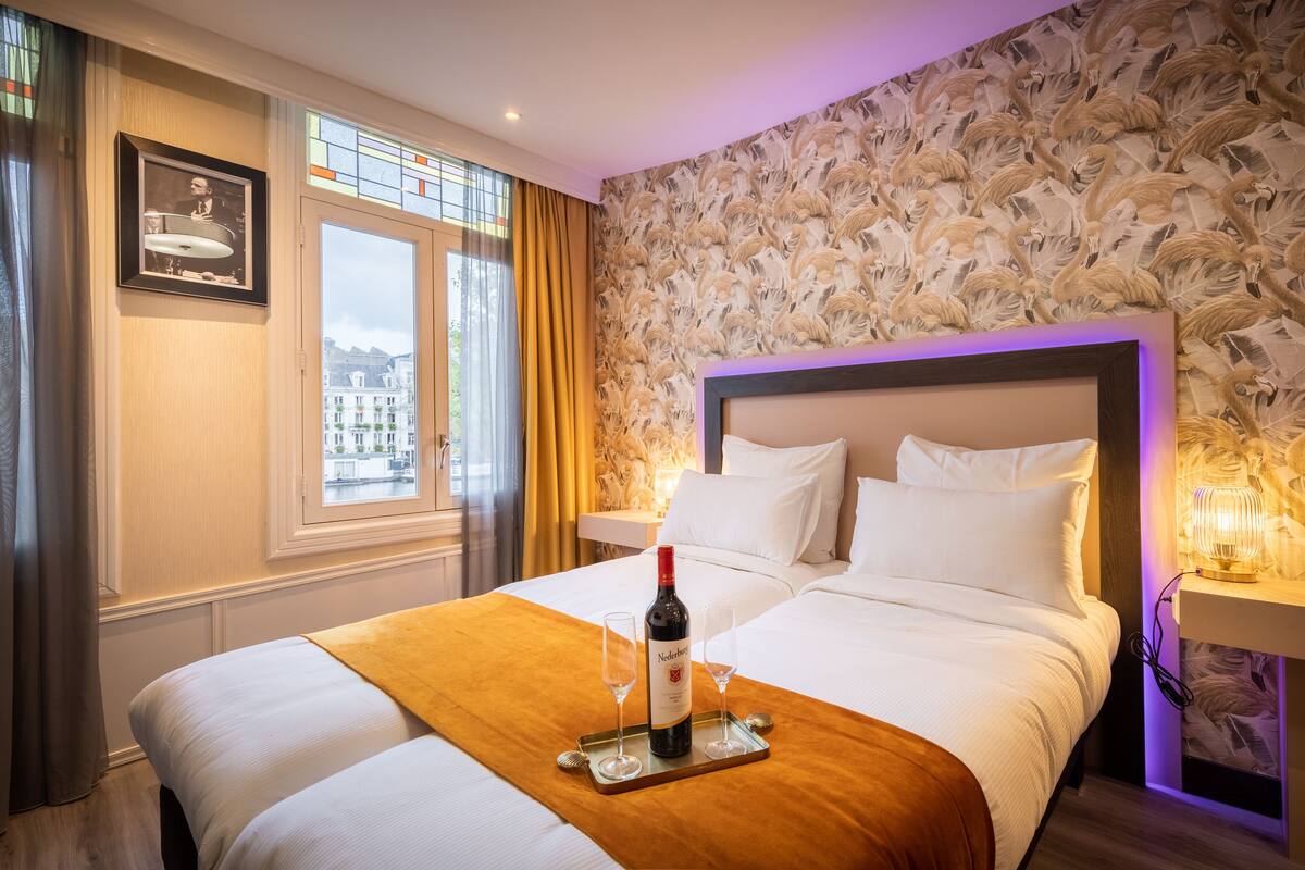 A hotel room with a large bed, a bottle of wine, and two glasses on a tray.