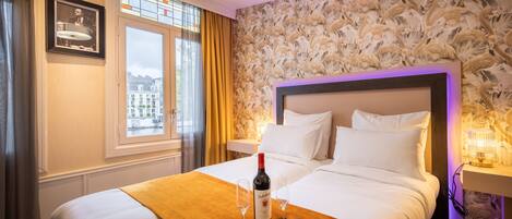 A hotel room with a large bed, a bottle of wine, and two glasses on a tray.