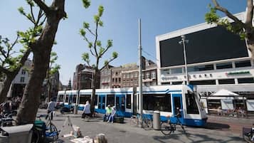 Una estación de tranvía con un edificio moderno al fondo, cielo despejado y algunas personas y bicicletas cerca.