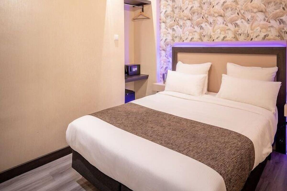 A hotel room with a bed, a ceiling light, an air conditioning unit, and a wall with a patterned design.