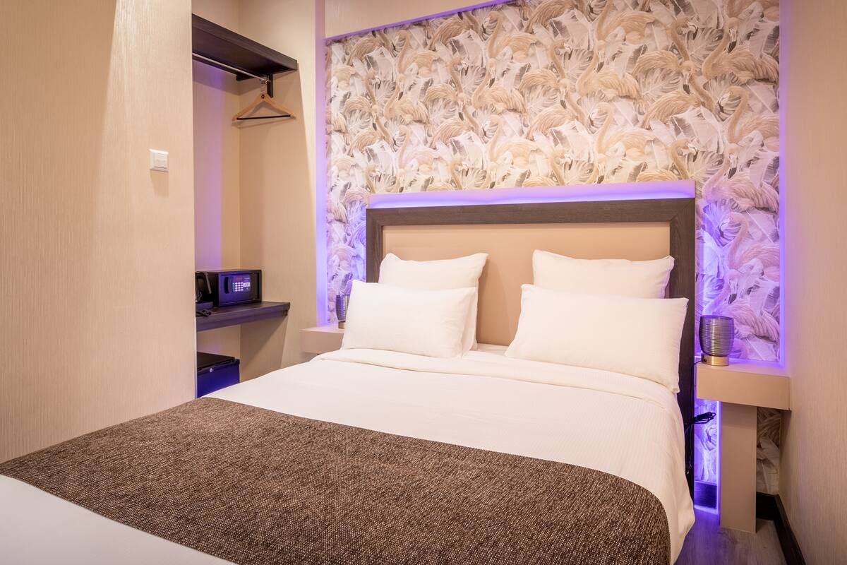 A hotel room with a large bed, a nightstand, a wall-mounted TV, and a decorative wall panel.
