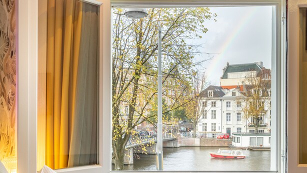 A hotel room with a bed, a window with curtains, a bottle of wine, and two glasses on a tray. - Hotel Oscar (Amsterdam)